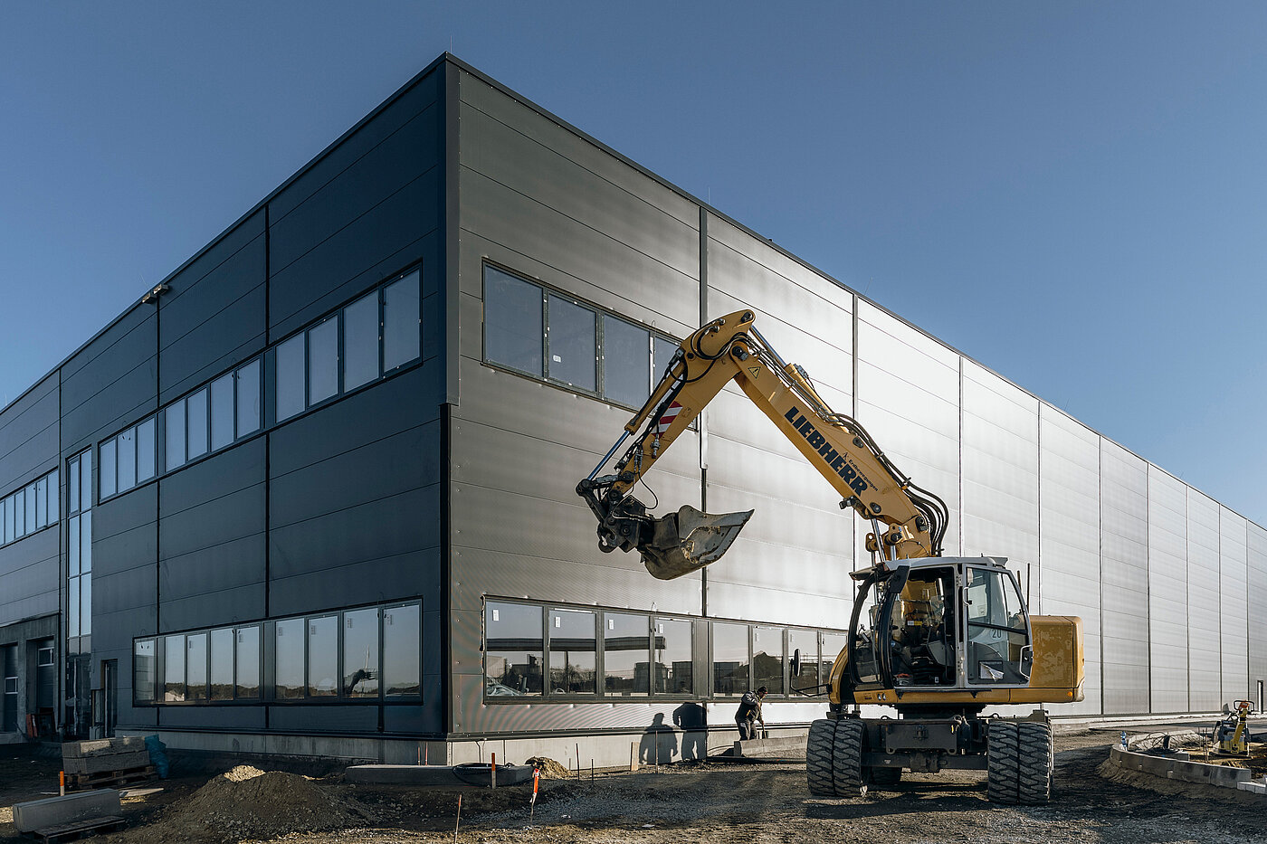 Newly constructed modern building with construction vehicle in the foreground, under a blue sky.