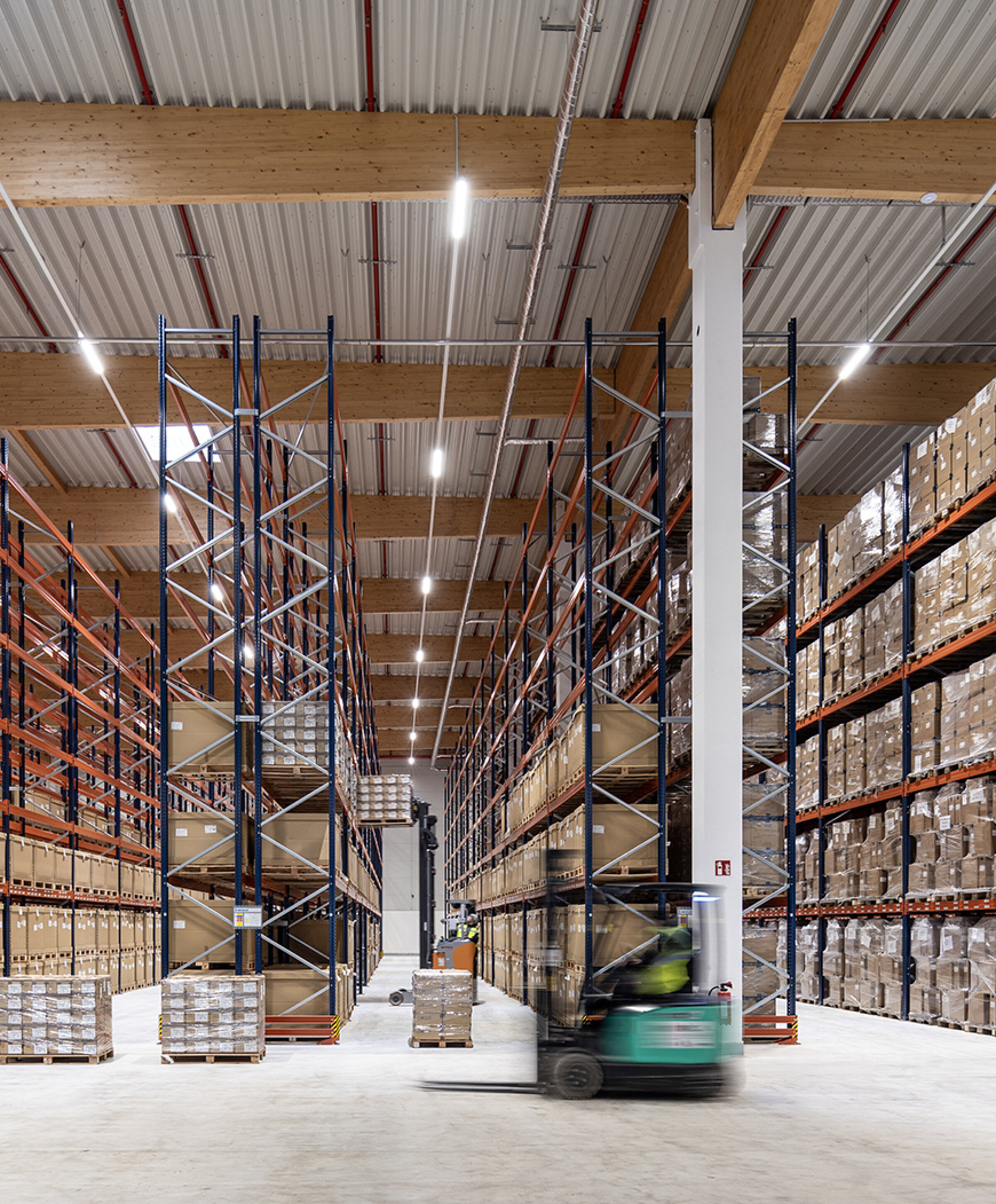 Großer Lagerraum mit hohen Regalen, gefüllt mit Kartons. Ein Gabelstapler fährt durch den Raum.