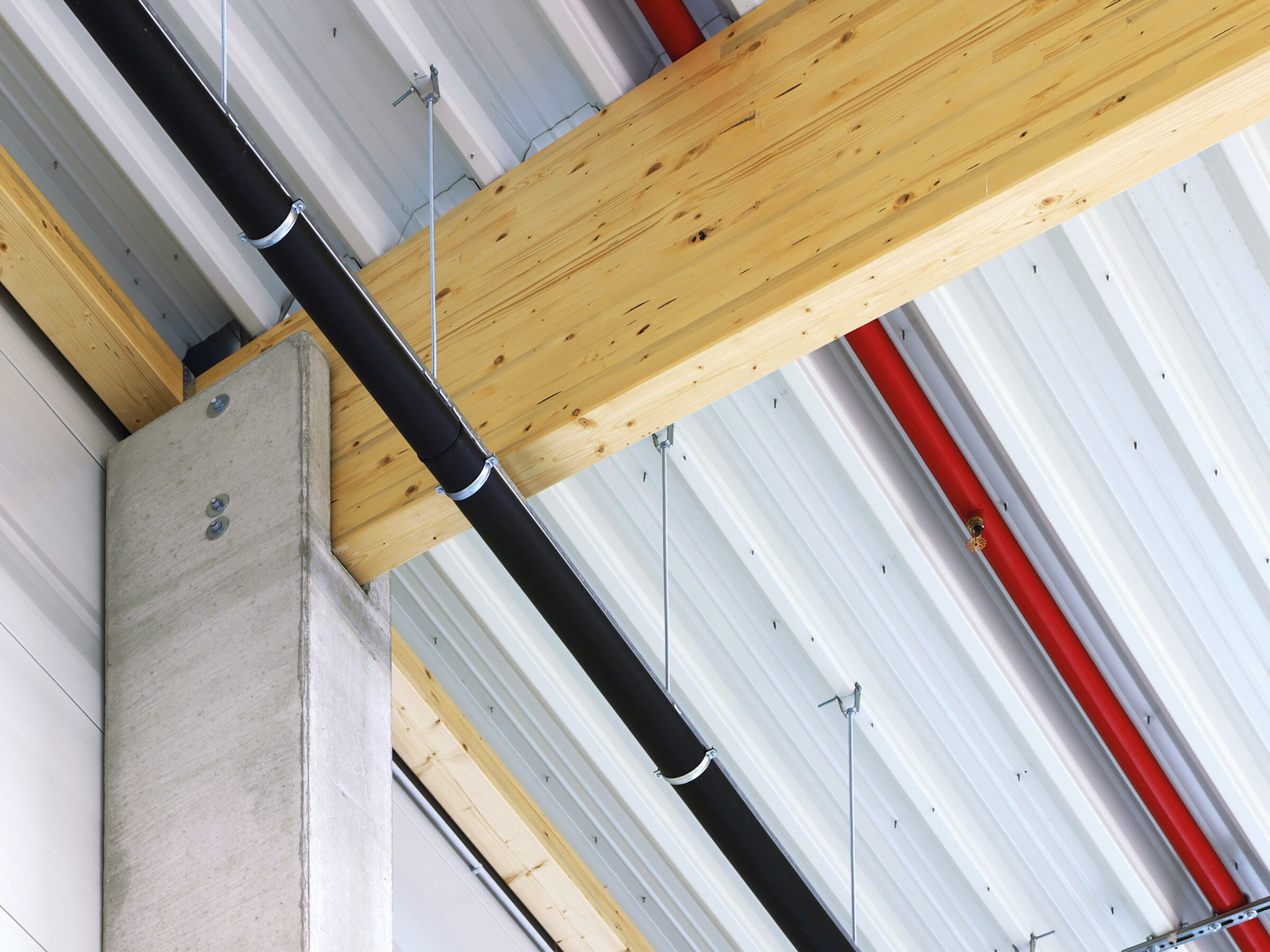 Holz- und Betonkonstruktion mit hängenden Rohren an einer Decke in einem modernen Gebäude.