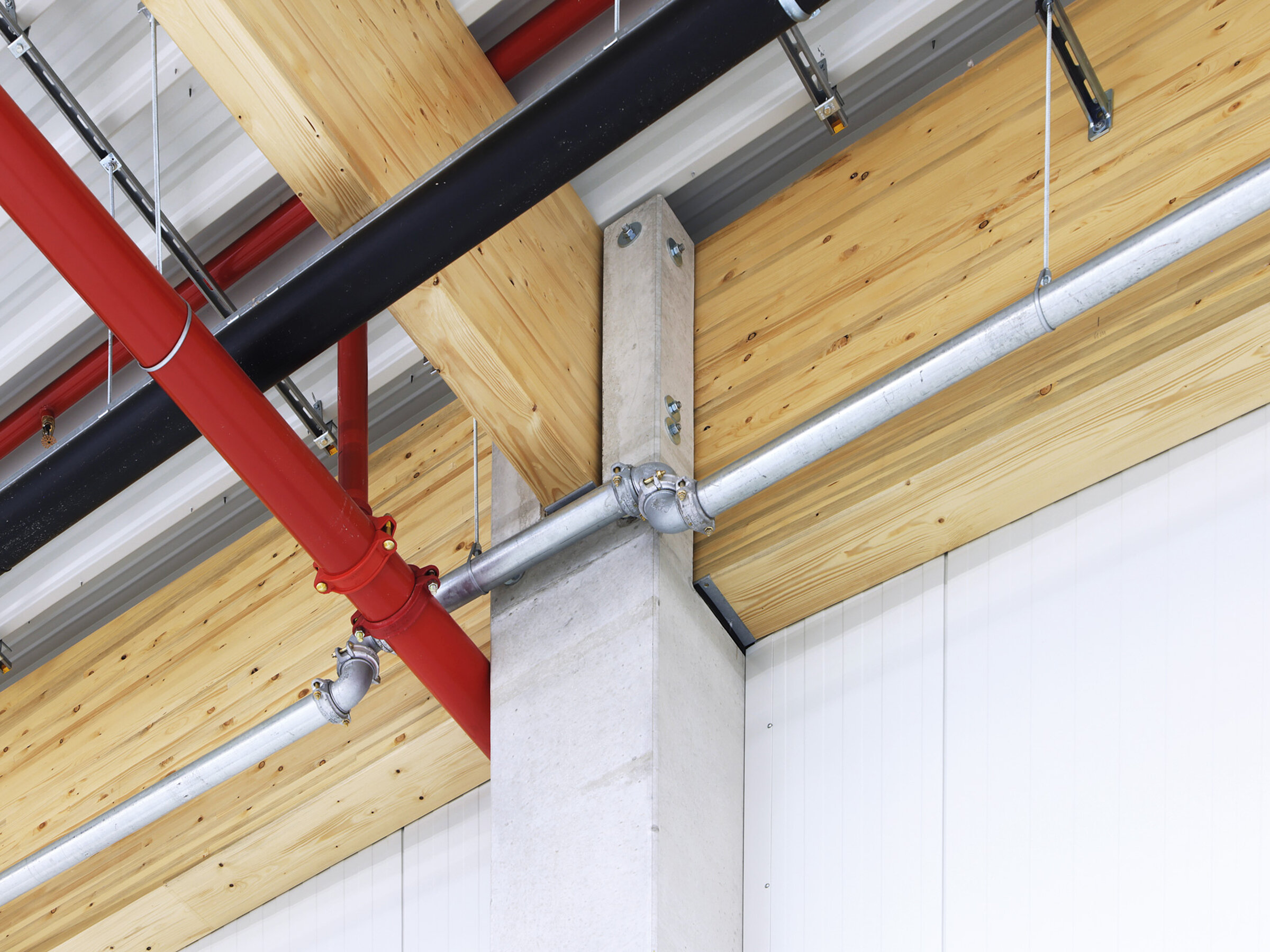 Detailansicht eines modernen Raumes mit Holz- und Metallkonstruktionen sowie sichtbaren Rohren an der Decke.