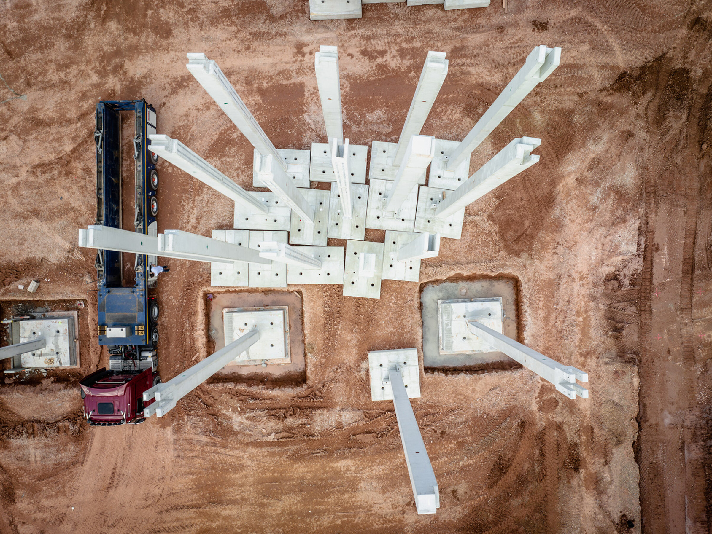 Bird's-eye view of a construction site with concrete pillars and a truck next to a pile of earth.