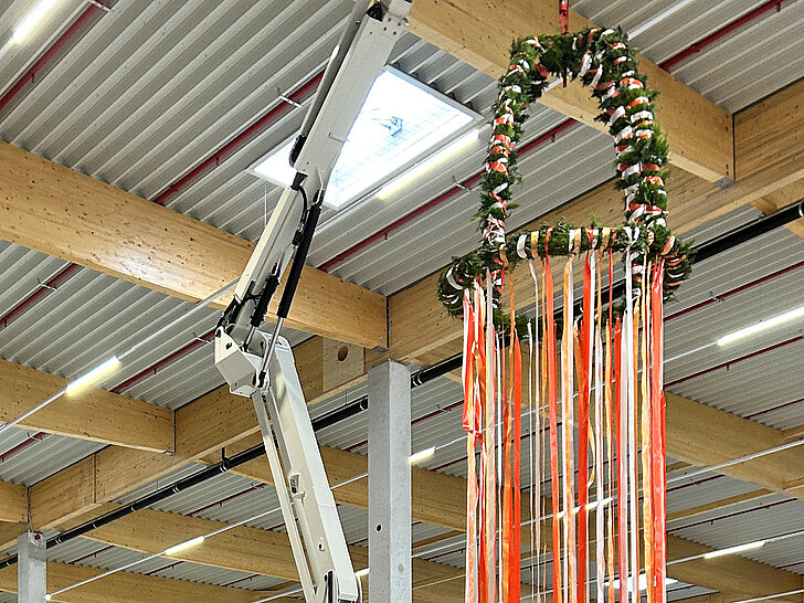 Ein Kran, der einen geschmückten Kranz mit bunten Bändern von der Decke eines modernen Gebäudes absenkt.