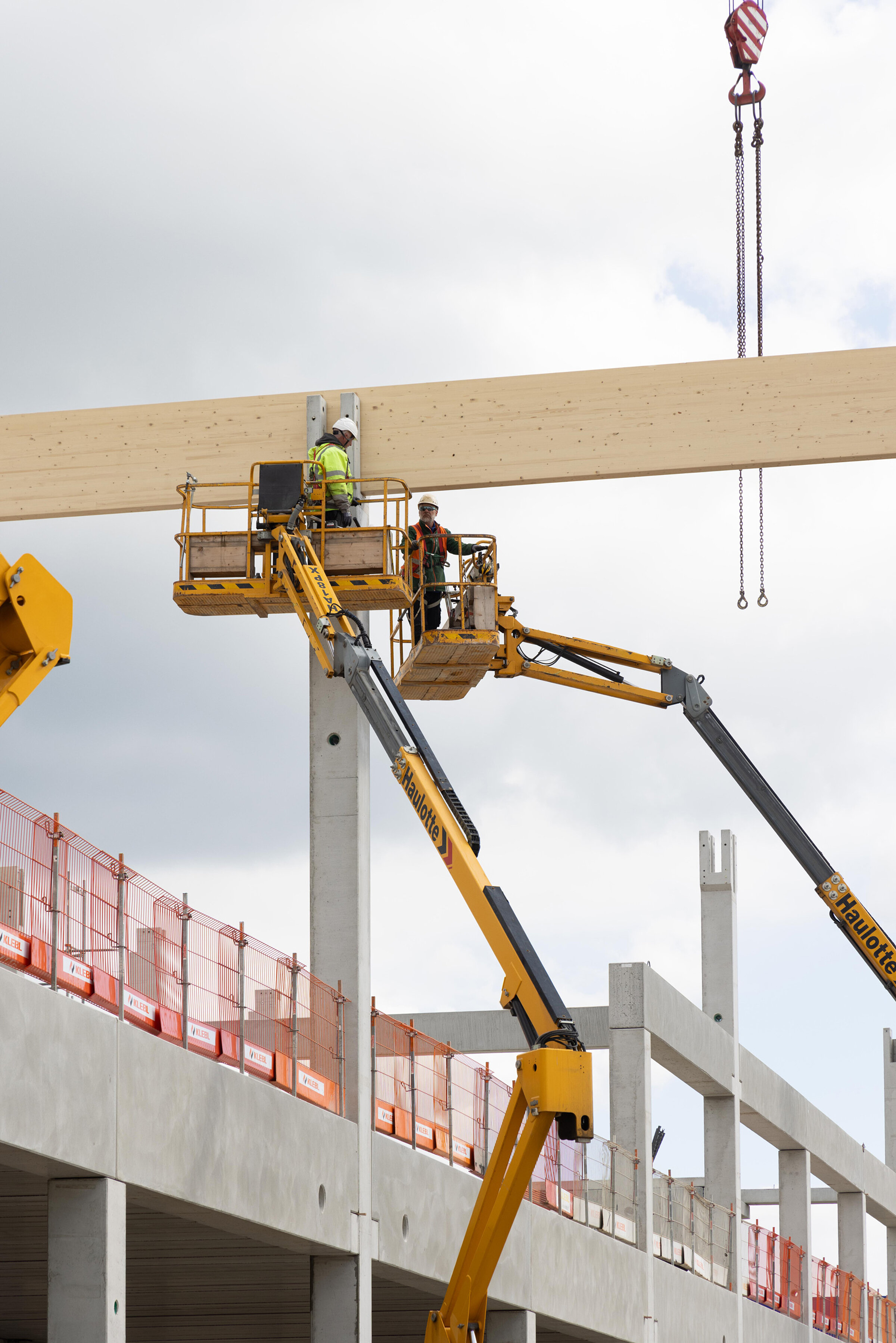 Two construction workers are working on a lifting platform on a wooden beam of a construction site building.