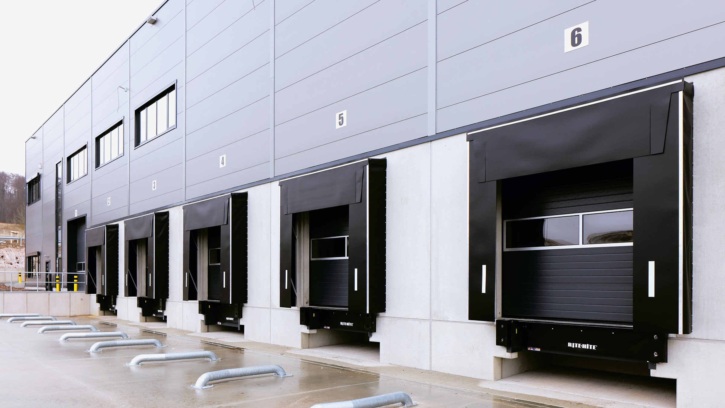 Moderne Lagerhalle mit mehreren Überladebrücken. Graue Sandwich-Fassade, schwarze Tore..