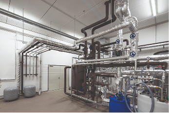 Industrieanlage mit metallenen Rohrleitungen, Ventilen und Tanks in einem Raum.