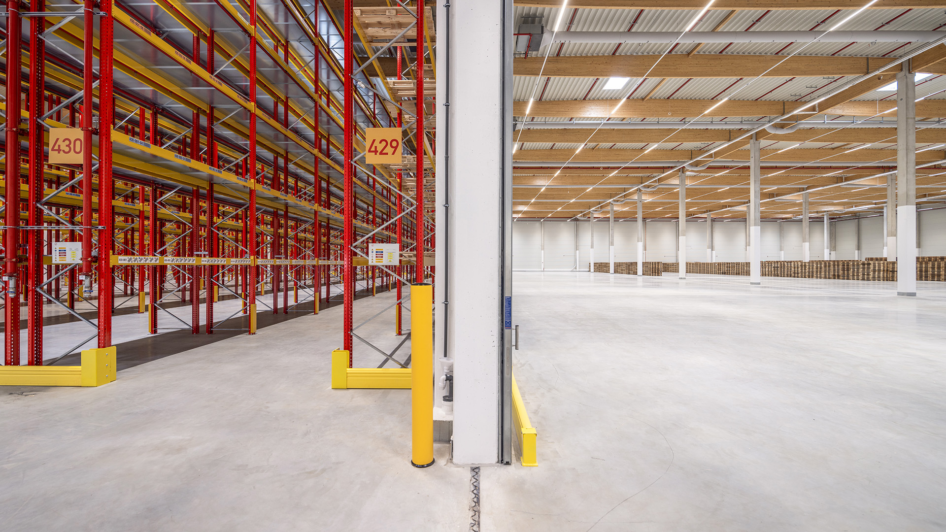 Ein moderner Lagerraum mit roten Regalen, gelben Sicherheitsmarkierungen und einem hellen, offenen Flächenlayout.